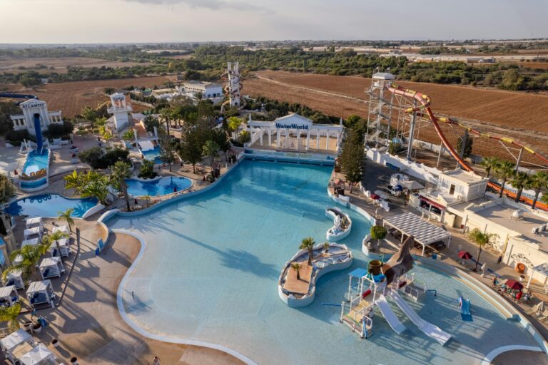 getaitrends - BEST WATERPARKS IN NIGERIA- Vibrant tropical resort scene featuring a pool, waterslide, and lush palm trees, ideal for summer vacations.
